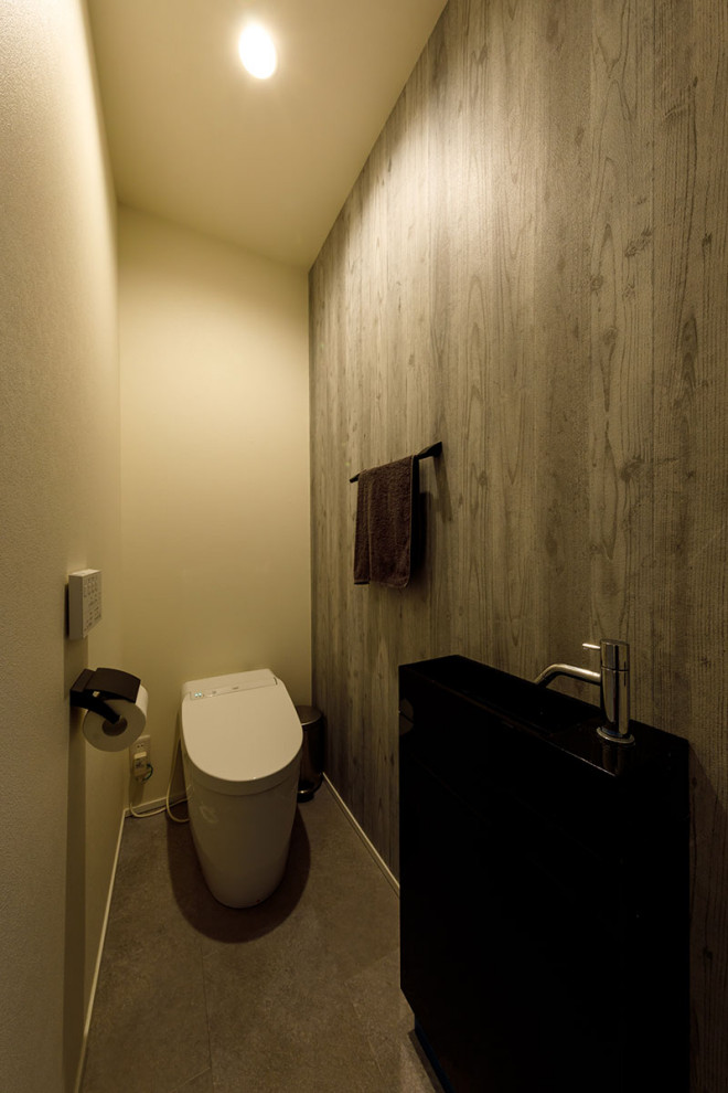 This is an example of a mid-sized powder room in Tokyo Suburbs with beaded inset cabinets, blue cabinets, a one-piece toilet, grey walls, porcelain floors, an integrated sink, solid surface benchtops, grey floor, black benchtops, a built-in vanity, wallpaper and wallpaper.