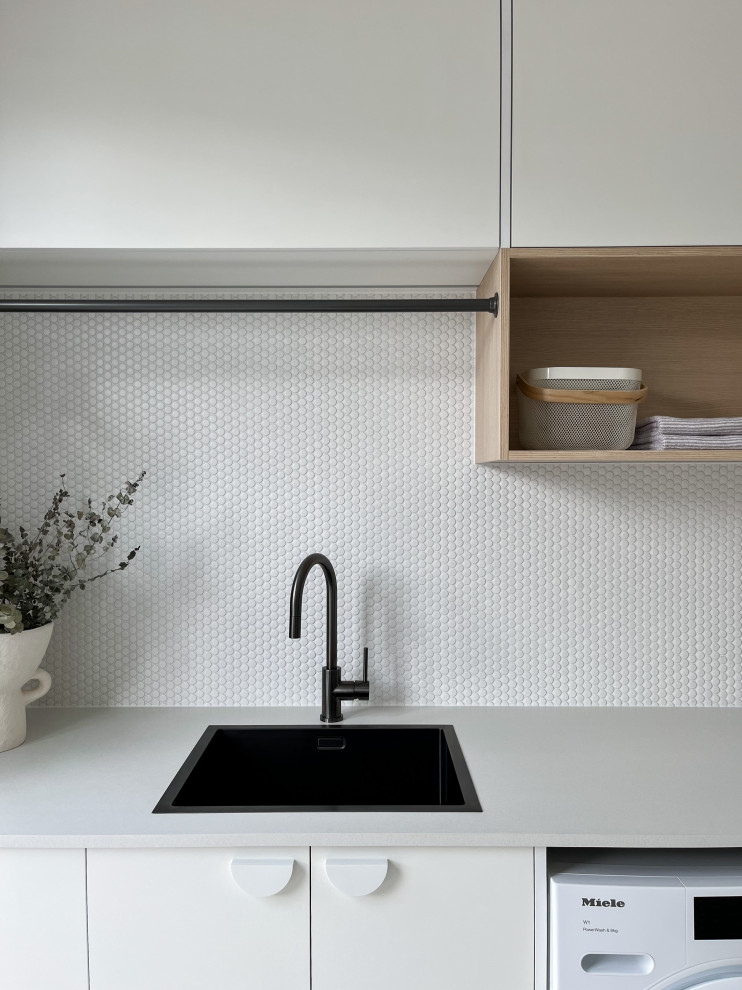 Exempel på en mellanstor modern vita linjär vitt tvättstuga enbart för tvätt, med en undermonterad diskho, släta luckor, vita skåp, laminatbänkskiva, vitt stänkskydd, stänkskydd i mosaik, vita väggar, klinkergolv i porslin, en tvättmaskin och torktumlare bredvid varandra och grått golv