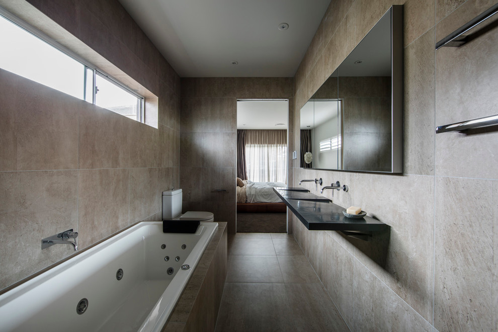 Photo of a mid-sized contemporary bathroom in Sydney with an undermount tub, a two-piece toilet, beige tile, stone slab, beige walls, cement tiles, an integrated sink and onyx benchtops.