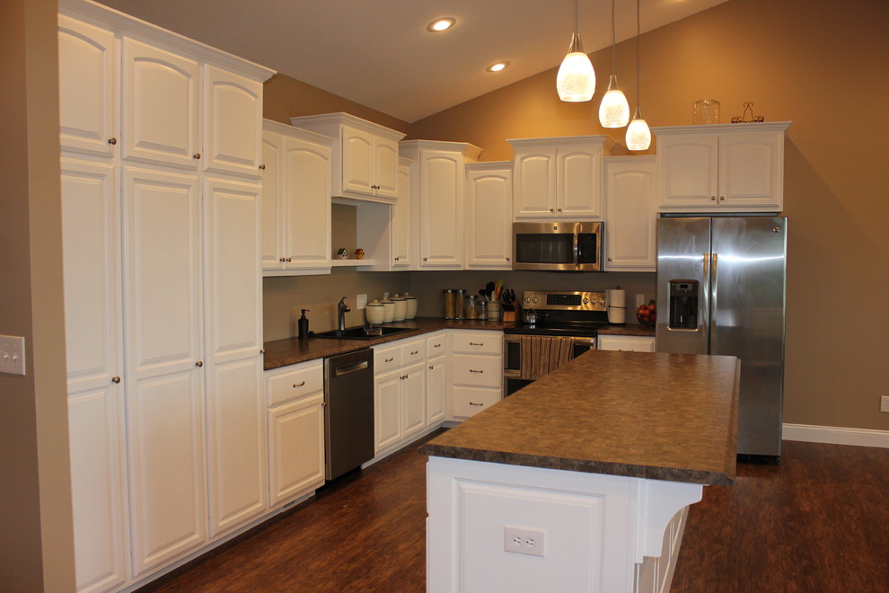 Inspiration for a mid-sized transitional l-shaped laminate floor and brown floor kitchen remodel in Chicago with a drop-in sink, raised-panel cabinets, white cabinets, laminate countertops, stainless steel appliances and an island