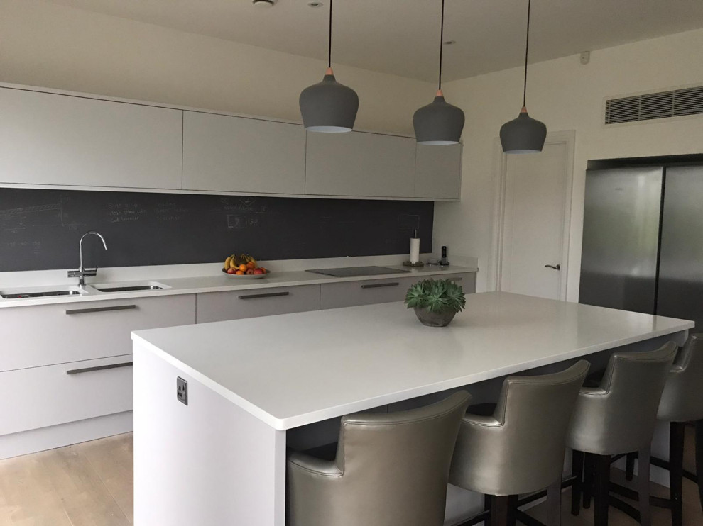 Photo of a modern eat-in kitchen in Buckinghamshire with recessed-panel cabinets, black splashback, slate splashback, with island and white benchtop.
