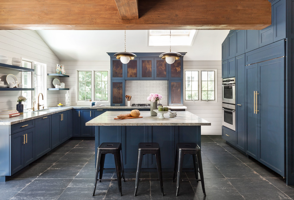 Photo of a beach style l-shaped kitchen in New York with an undermount sink, shaker cabinets, blue cabinets, white splashback, panelled appliances, with island, black floor and multi-coloured benchtop.