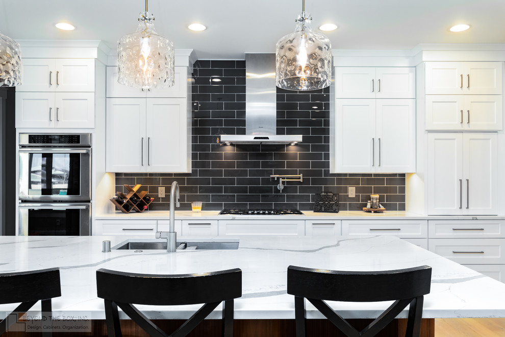 Photo of a mid-sized modern l-shaped eat-in kitchen in Denver with an undermount sink, shaker cabinets, white cabinets, quartz benchtops, black splashback, ceramic splashback, stainless steel appliances, light hardwood floors, with island, beige floor and multi-coloured benchtop.