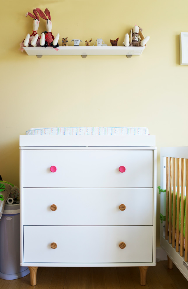 Mid-sized scandinavian nursery in New York with yellow walls and light hardwood floors for girls.
