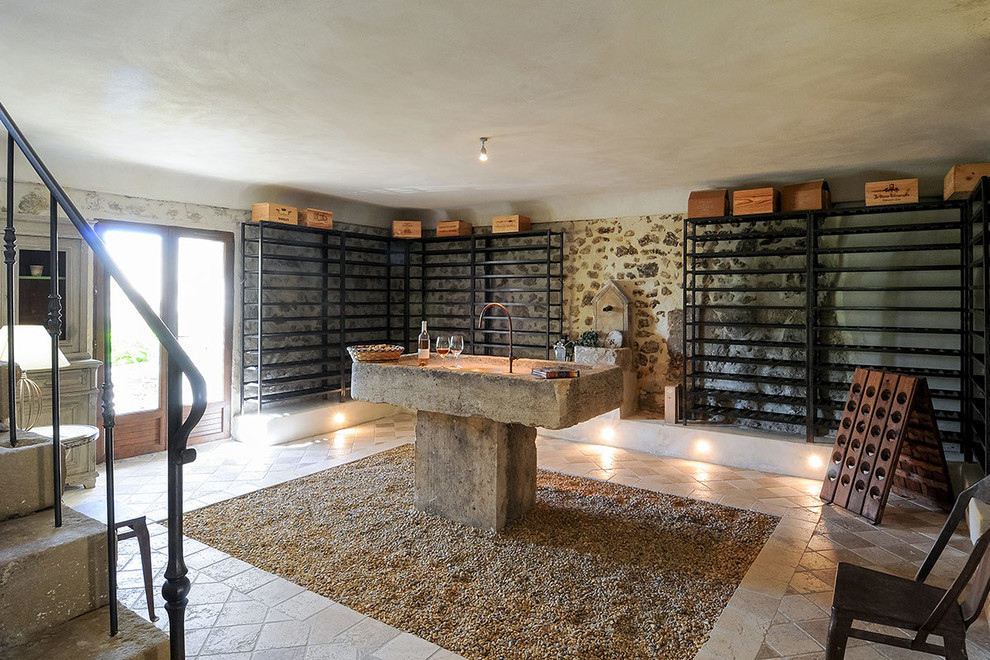 Photo of a mid-sized country wine cellar with limestone floors, storage racks and beige floor.