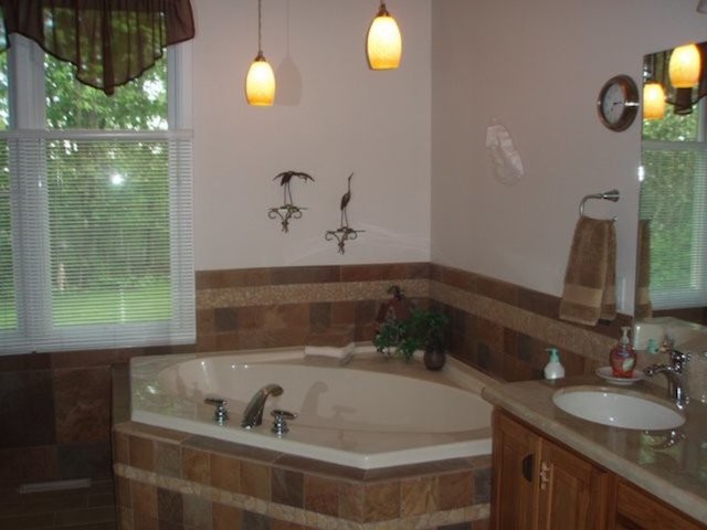 Corner bathtub - transitional beige tile corner bathtub idea with an undermount sink, medium tone wood cabinets, granite countertops and beige walls