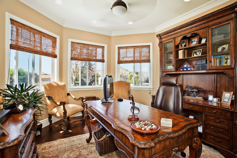 This is an example of a traditional home office in San Diego with beige walls, dark hardwood floors and a freestanding desk.