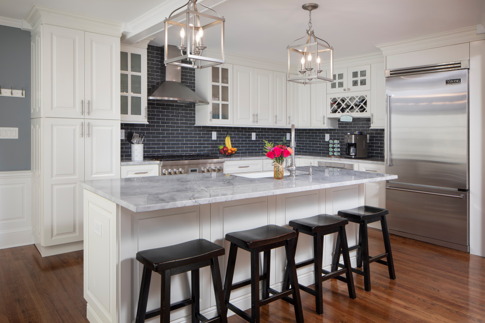 Transitional u-shaped medium tone wood floor, brown floor and exposed beam open concept kitchen photo in New York with an undermount sink, raised-panel cabinets, marble countertops, black backsplash, subway tile backsplash, stainless steel appliances, an island and gray countertops