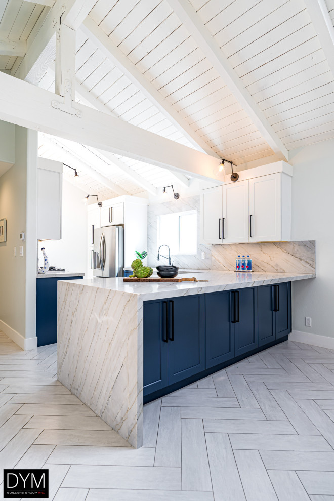 Inspiration for a beach style galley eat-in kitchen in Los Angeles with a farmhouse sink, shaker cabinets, blue cabinets, quartz benchtops, white splashback, engineered quartz splashback, stainless steel appliances, a peninsula, white floor, white benchtop, vaulted and light hardwood floors.