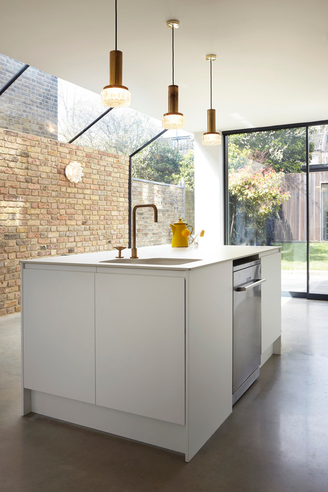 This is an example of a small contemporary single-wall open plan kitchen with a belfast sink, flat-panel cabinets, white cabinets, composite countertops, white splashback, glass sheet splashback, white appliances, concrete flooring and an island.