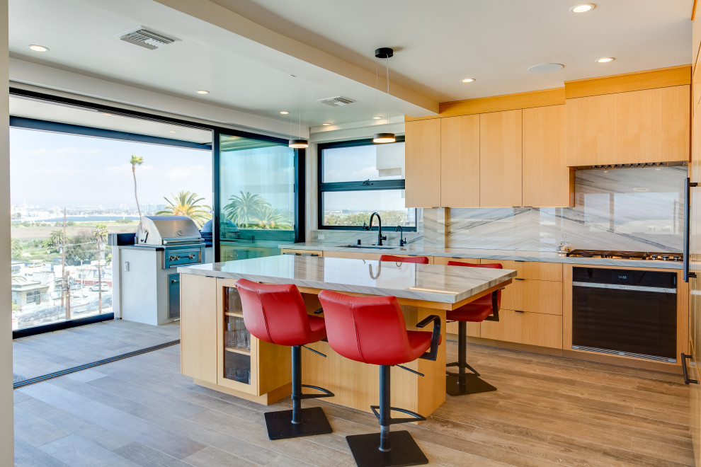 This is an example of a mid-sized contemporary l-shaped kitchen in Los Angeles with flat-panel cabinets, light wood cabinets, quartzite benchtops, porcelain floors, with island, a single-bowl sink, grey splashback, glass sheet splashback, black appliances, brown floor and grey benchtop.