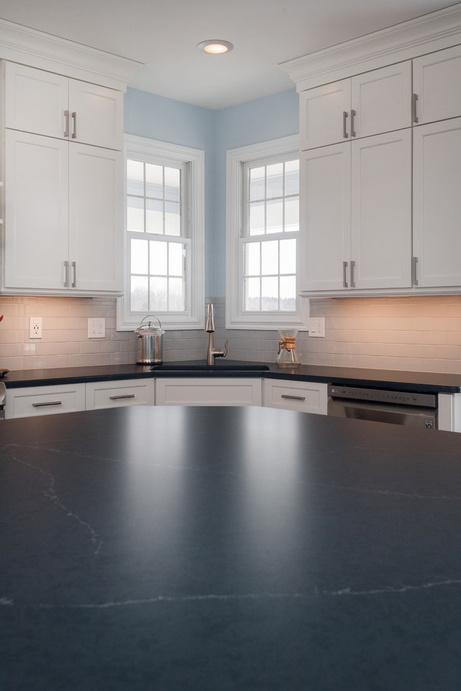 Example of a large transitional u-shaped medium tone wood floor and brown floor eat-in kitchen design with an undermount sink, shaker cabinets, white cabinets, quartz countertops, white backsplash, ceramic backsplash, stainless steel appliances and an island