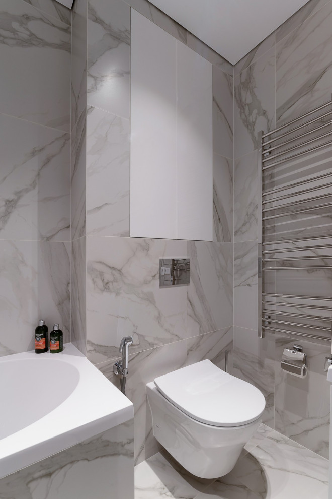 Foto på ett mellanstort funkis vit en-suite badrum, med släta luckor, vita skåp, ett badkar i en alkov, en dusch/badkar-kombination, en vägghängd toalettstol, grå kakel, porslinskakel, grå väggar, klinkergolv i porslin, ett fristående handfat, bänkskiva i akrylsten, grått golv och med dusch som är öppen