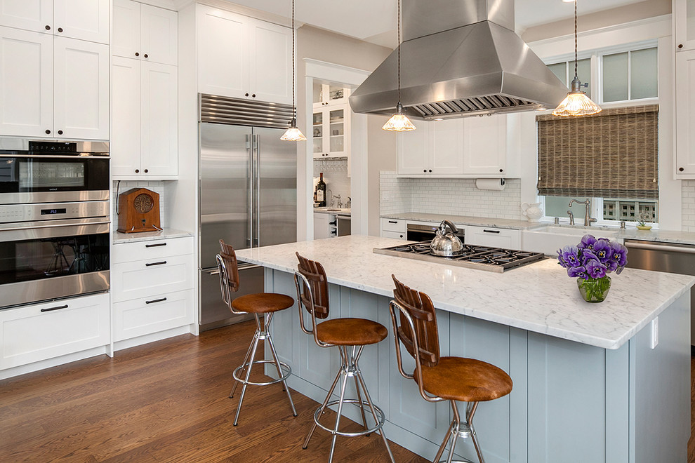 This is an example of a country kitchen in Seattle with a farmhouse sink, shaker cabinets, white cabinets, marble benchtops, white splashback, subway tile splashback, stainless steel appliances, with island and medium hardwood floors.