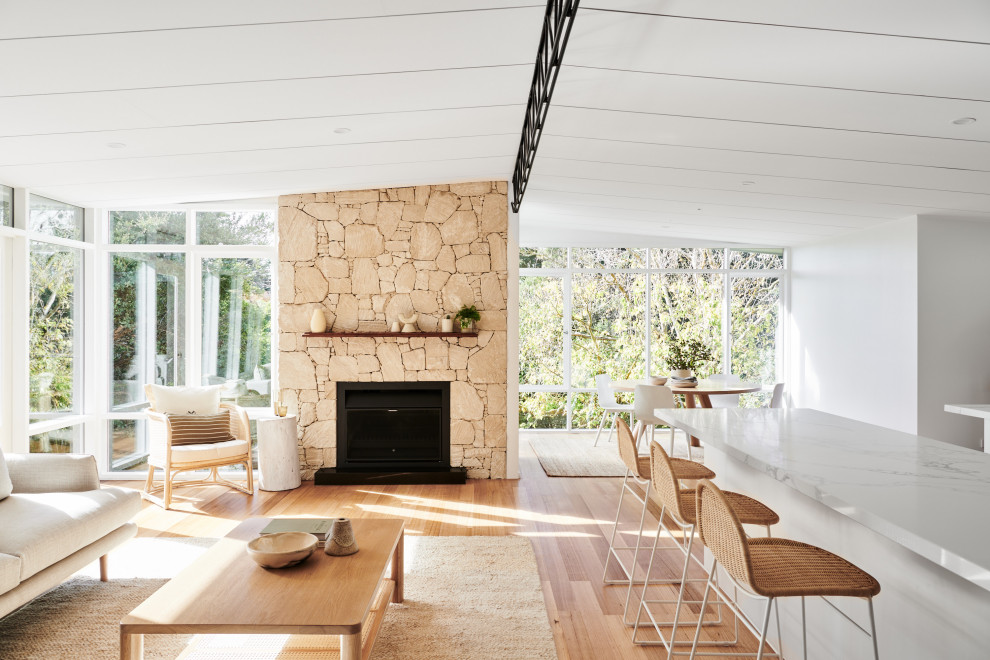 Photo of a mid-sized beach style open concept living room in Melbourne with white walls, light hardwood floors, a standard fireplace, a stone fireplace surround and brown floor.