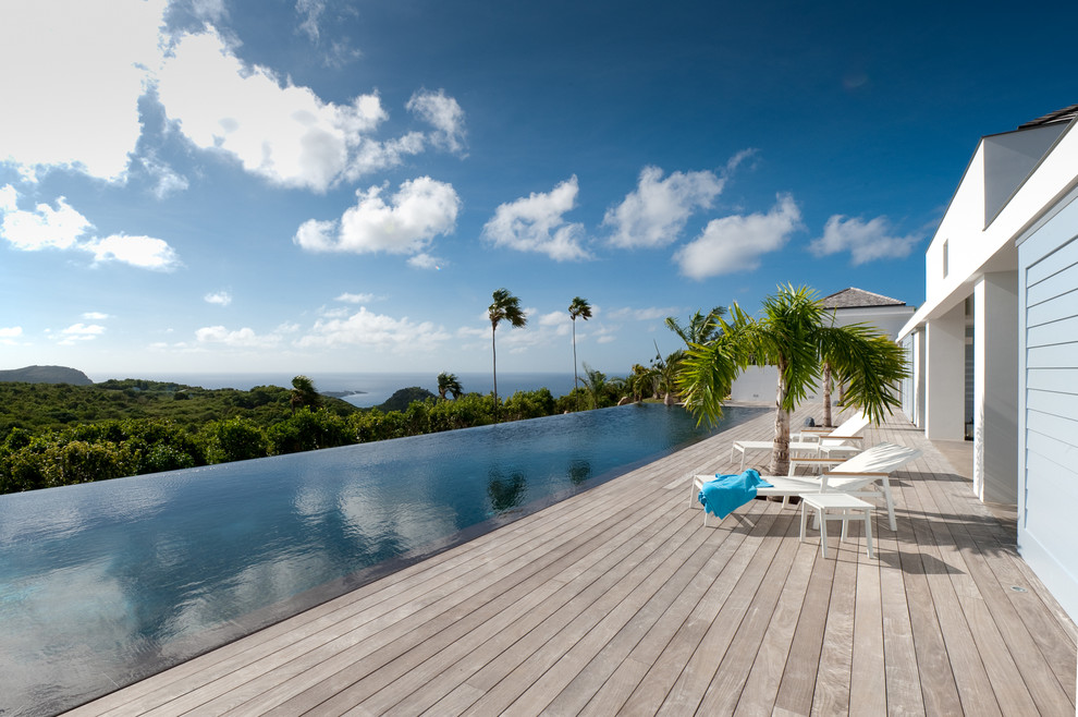 Expansive tropical backyard rectangular infinity pool in Other with decking.
