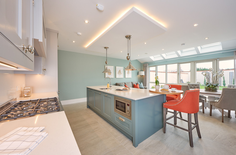 This is an example of a mid-sized transitional single-wall open plan kitchen in Dublin with recessed-panel cabinets, blue cabinets, white splashback, with island, grey floor, an undermount sink and stainless steel appliances.
