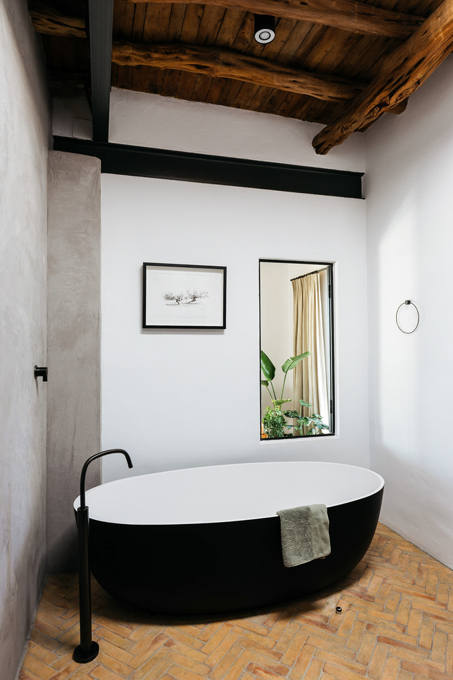 Mediterranean bathroom in Other with a freestanding tub, white walls, brick floors and brown floor.