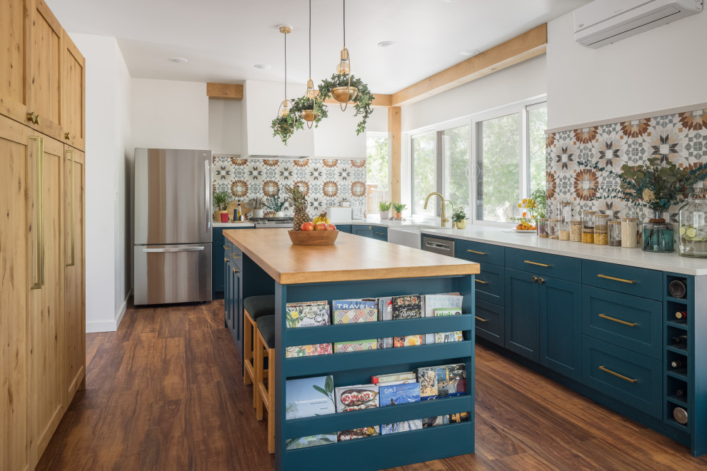 Photo of a mid-sized l-shaped eat-in kitchen in Other with a farmhouse sink, shaker cabinets, blue cabinets, wood benchtops, multi-coloured splashback, ceramic splashback, stainless steel appliances, medium hardwood floors, with island, white benchtop and exposed beam.