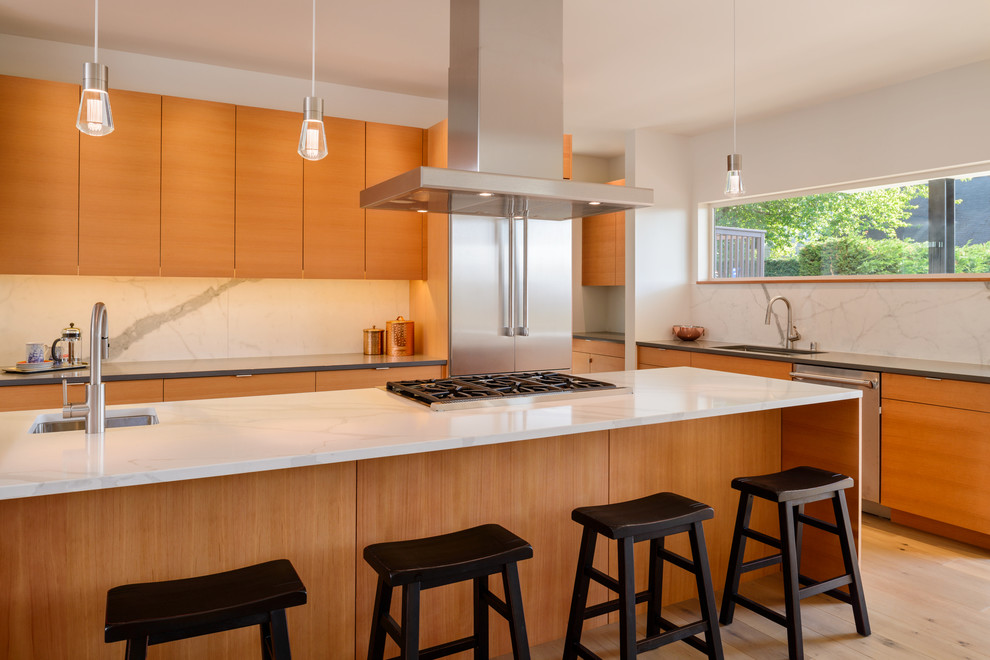 Photo of a large contemporary l-shaped eat-in kitchen in Seattle with a single-bowl sink, flat-panel cabinets, light wood cabinets, quartz benchtops, white splashback, stone slab splashback, stainless steel appliances, light hardwood floors, with island and white benchtop.