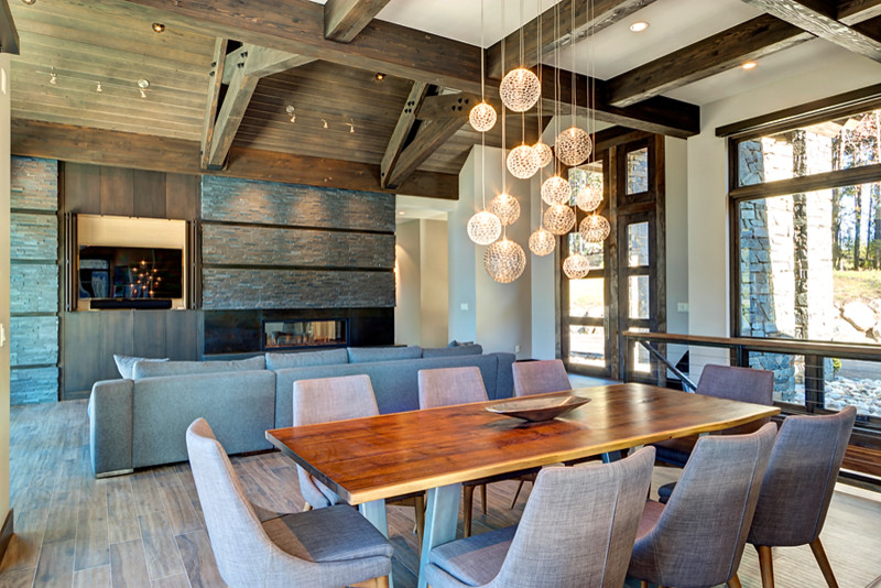 Design ideas for a large midcentury open plan dining in Denver with beige walls, medium hardwood floors, a two-sided fireplace, a stone fireplace surround and brown floor.