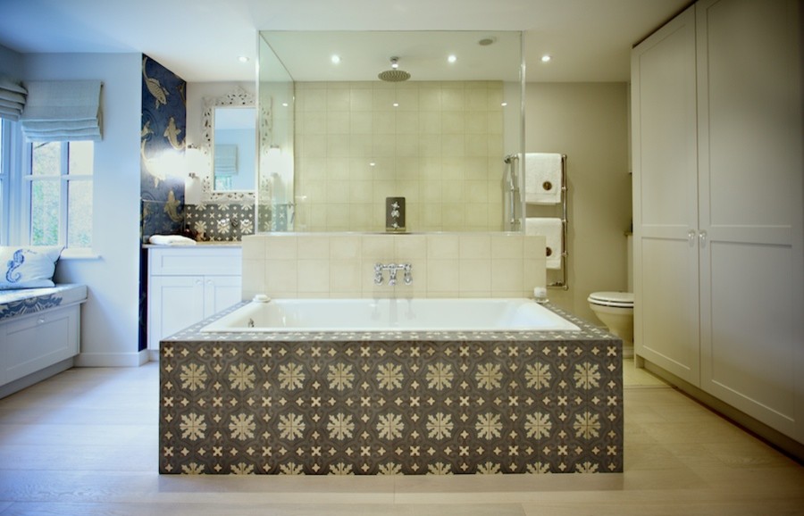 This is an example of a large eclectic master bathroom in Sussex with a drop-in sink, shaker cabinets, white cabinets, limestone benchtops, a drop-in tub, a double shower, a wall-mount toilet, multi-coloured tile, cement tile, grey walls and light hardwood floors.