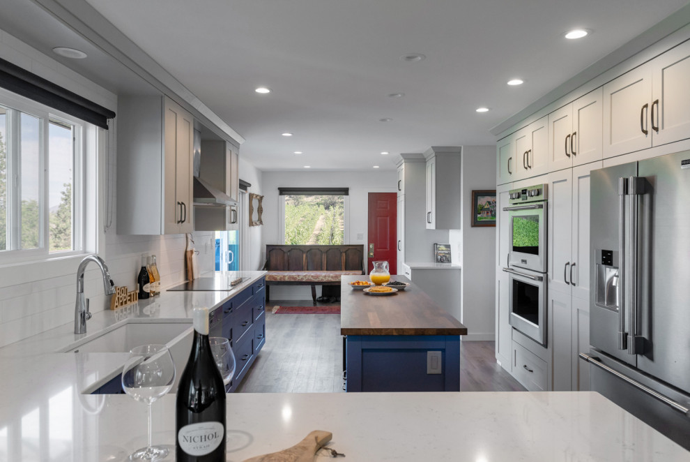 Eat-in kitchen - mid-sized transitional u-shaped medium tone wood floor and brown floor eat-in kitchen idea with recessed-panel cabinets, gray cabinets, quartz countertops, white backsplash, ceramic backsplash, stainless steel appliances, an island and white countertops