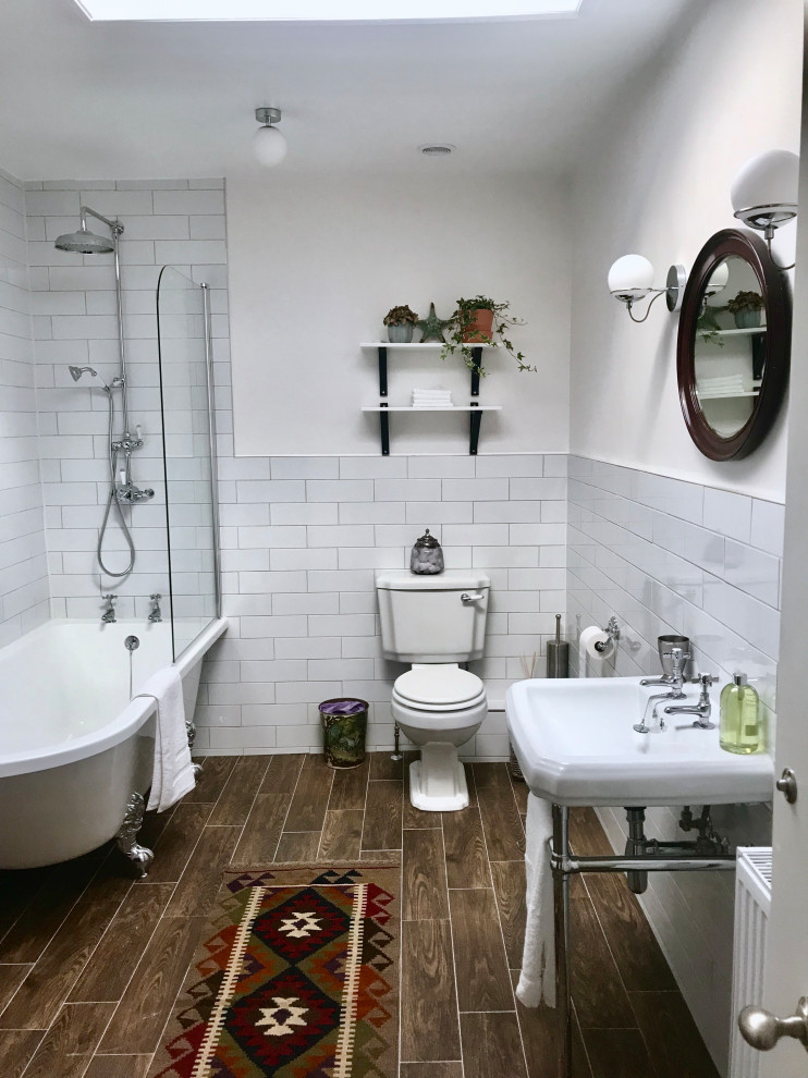 Design ideas for a mid-sized traditional kids bathroom in Gloucestershire with white cabinets, a freestanding tub, a shower/bathtub combo, a one-piece toilet, white tile, ceramic tile, yellow walls, ceramic floors, a pedestal sink, brown floor, a hinged shower door, a niche, a single vanity and a freestanding vanity.