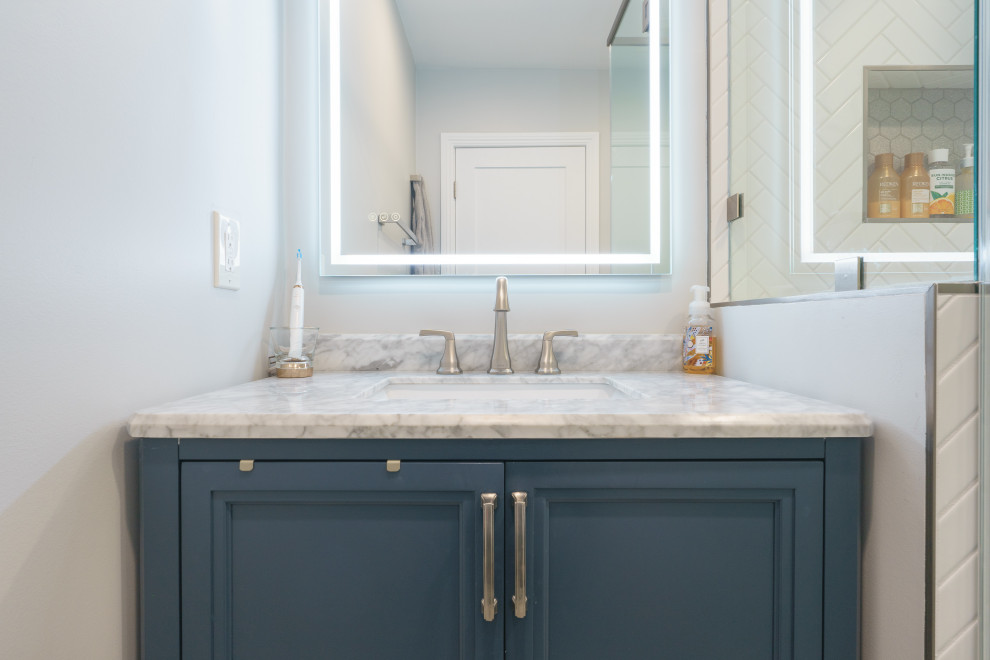 This is an example of a small modern ensuite bathroom in Los Angeles with raised-panel cabinets, blue cabinets, a corner shower, a two-piece toilet, white tiles, ceramic tiles, grey walls, light hardwood flooring, a built-in sink, marble worktops, grey floors, a hinged door, white worktops, a shower bench, a single sink and a built in vanity unit.