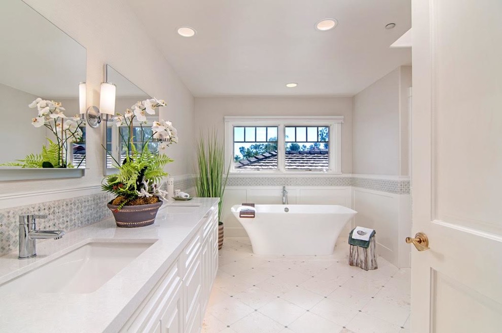 Photo of a large transitional master bathroom in San Diego with raised-panel cabinets, white cabinets, a freestanding tub, a double shower, a one-piece toilet, white tile, stone tile, white walls, limestone floors, an undermount sink, engineered quartz benchtops and white floor.