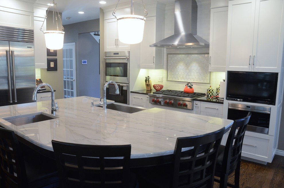 This is an example of a large transitional l-shaped eat-in kitchen in Grand Rapids with a farmhouse sink, white cabinets, white splashback, stainless steel appliances, with island, shaker cabinets, marble benchtops, subway tile splashback and dark hardwood floors.