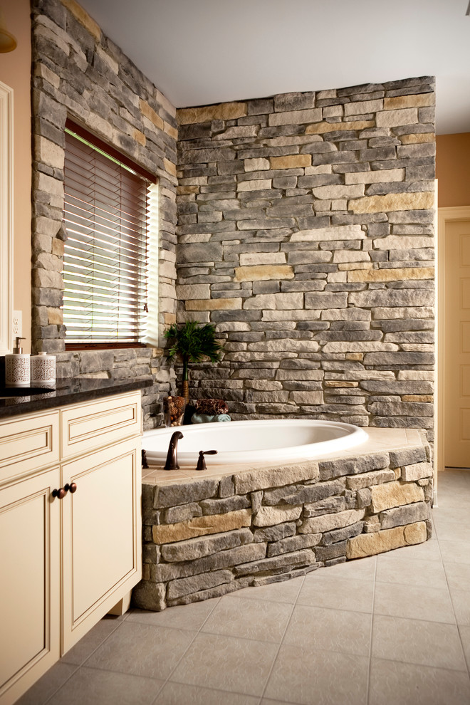 Inspiration for a large country master bathroom in Cleveland with raised-panel cabinets, beige cabinets, a drop-in tub, beige tile, stone tile, brown walls, porcelain floors, an undermount sink, engineered quartz benchtops and beige floor.