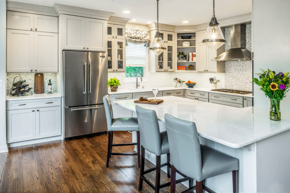 Inspiration for a mid-sized transitional u-shaped medium tone wood floor eat-in kitchen remodel in Chicago with an undermount sink, shaker cabinets, gray cabinets, quartz countertops, white backsplash, stone tile backsplash, stainless steel appliances, a peninsula and white countertops
