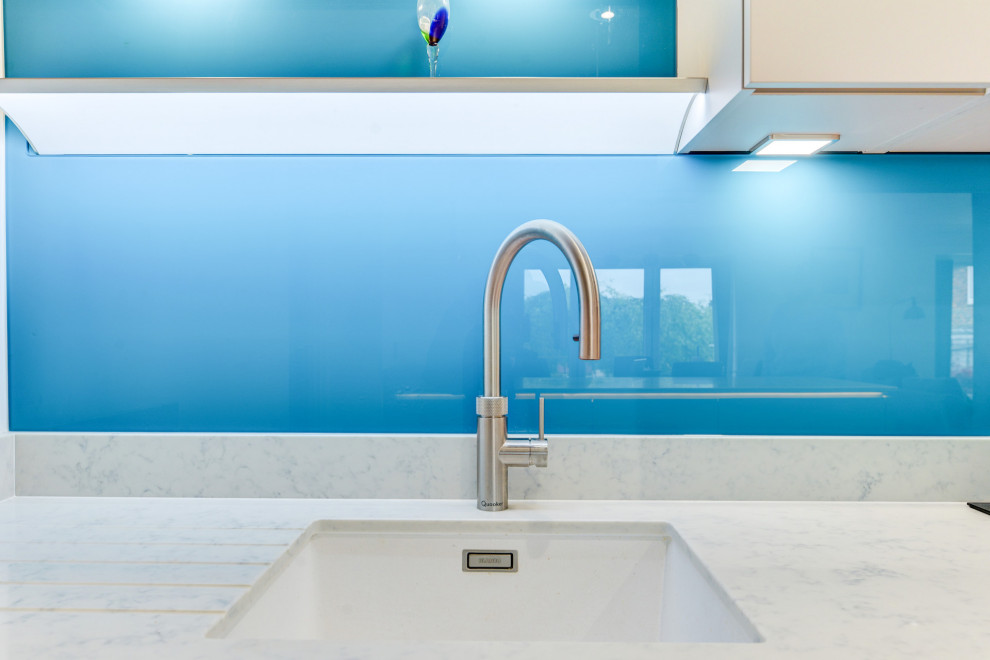 Esempio di una cucina minimalista di medie dimensioni con lavello sottopiano, ante lisce, ante grigie, top in quarzite, paraspruzzi blu, paraspruzzi con lastra di vetro, elettrodomestici da incasso, pavimento in vinile, pavimento marrone e top bianco