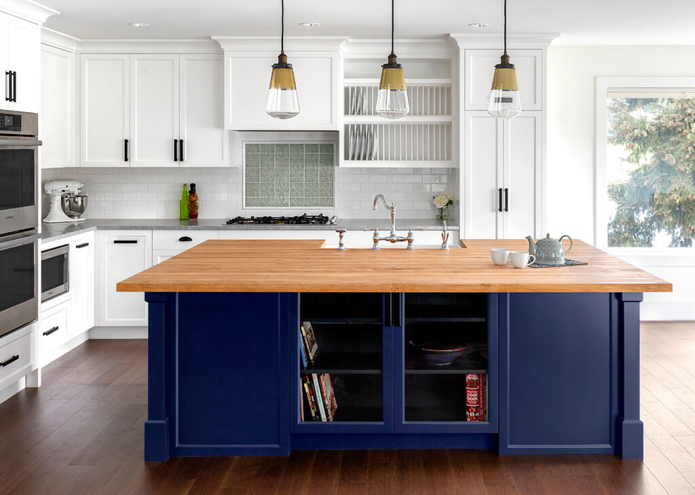 Beach style l-shaped medium tone wood floor kitchen photo with shaker cabinets, an island, white cabinets, white backsplash, subway tile backsplash, stainless steel appliances and gray countertops