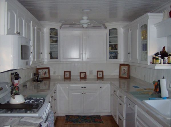 Mid-sized u-shaped medium tone wood floor eat-in kitchen photo with a double-bowl sink, white cabinets, marble countertops, white backsplash, white appliances and no island