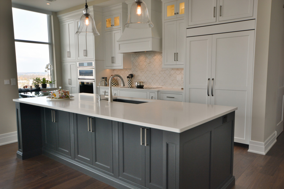 Example of a transitional single-wall medium tone wood floor and brown floor open concept kitchen design in Toronto with an undermount sink, shaker cabinets, white cabinets, quartz countertops, white backsplash, marble backsplash, paneled appliances, an island and white countertops