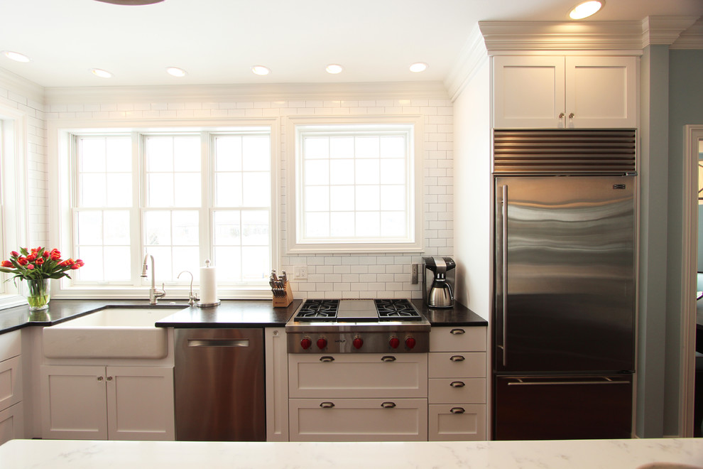 Example of a large transitional u-shaped medium tone wood floor and brown floor eat-in kitchen design with a farmhouse sink, recessed-panel cabinets, white cabinets, quartz countertops, white backsplash, porcelain backsplash, stainless steel appliances and an island