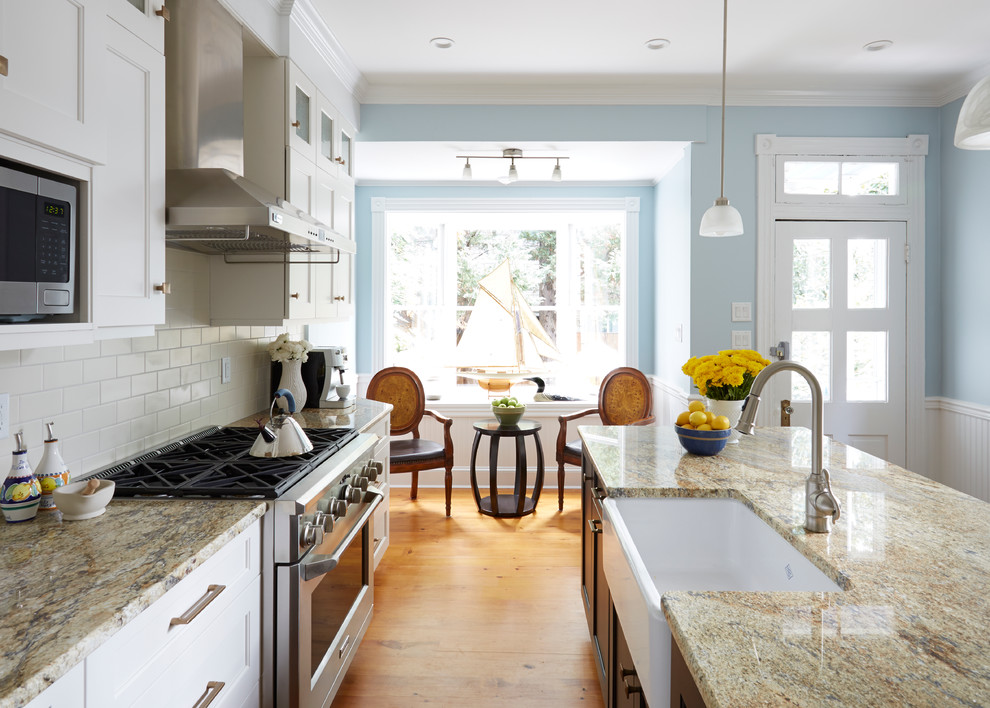 Example of a transitional medium tone wood floor eat-in kitchen design in DC Metro with a farmhouse sink, recessed-panel cabinets, white cabinets, granite countertops, white backsplash, subway tile backsplash, stainless steel appliances and an island