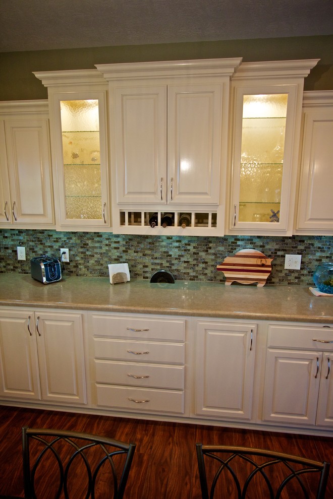Example of a large u-shaped medium tone wood floor open concept kitchen design with a drop-in sink, raised-panel cabinets, white cabinets, multicolored backsplash, glass tile backsplash, stainless steel appliances and an island