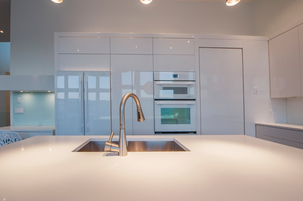 Photo of a modern open plan kitchen in Vancouver with a double-bowl sink, flat-panel cabinets, white cabinets, glass sheet splashback, white appliances, medium hardwood floors and with island.