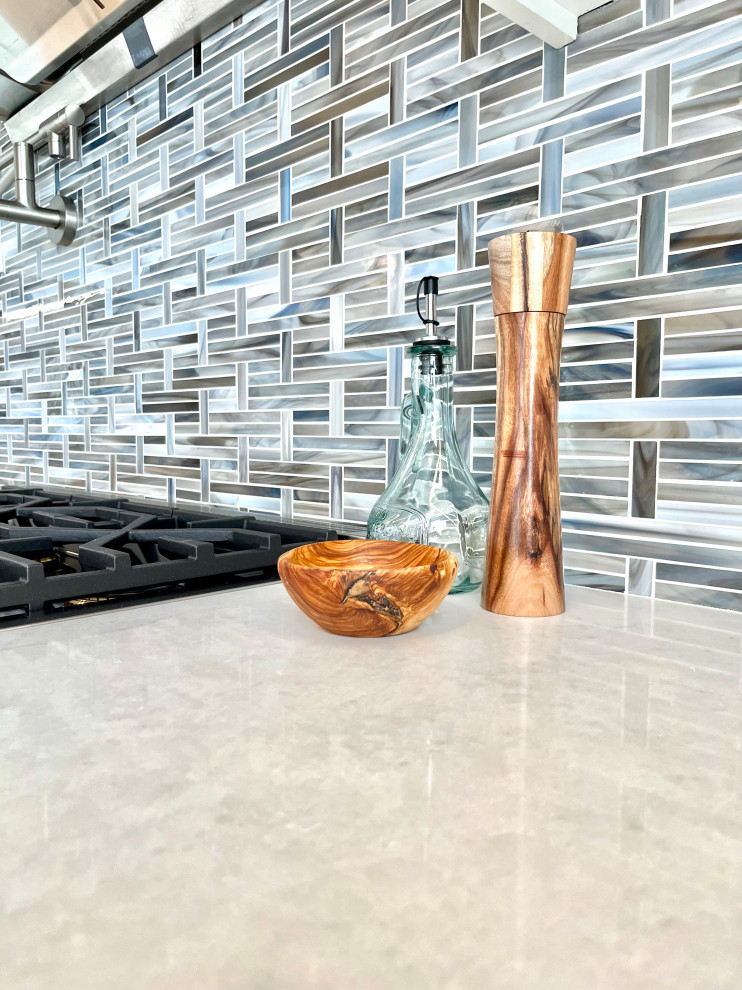 Inspiration for a transitional single-wall vinyl floor, brown floor and vaulted ceiling eat-in kitchen remodel with an undermount sink, shaker cabinets, white cabinets, quartz countertops, blue backsplash, glass sheet backsplash, stainless steel appliances, an island and gray countertops