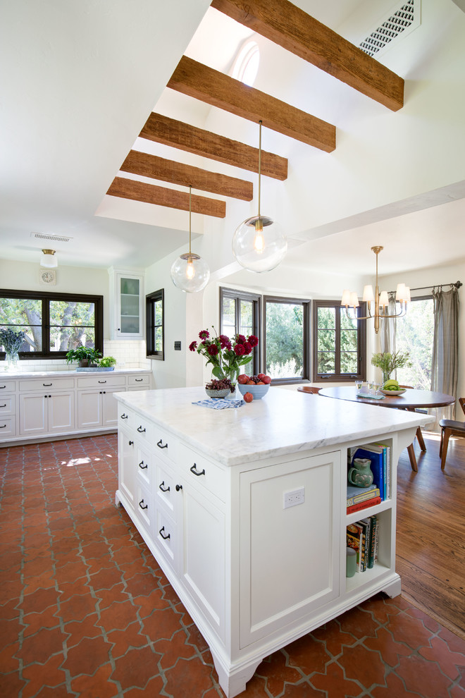Large mediterranean l-shaped eat-in kitchen in Los Angeles with white cabinets, marble benchtops, white splashback, terra-cotta floors, with island, orange floor and shaker cabinets.