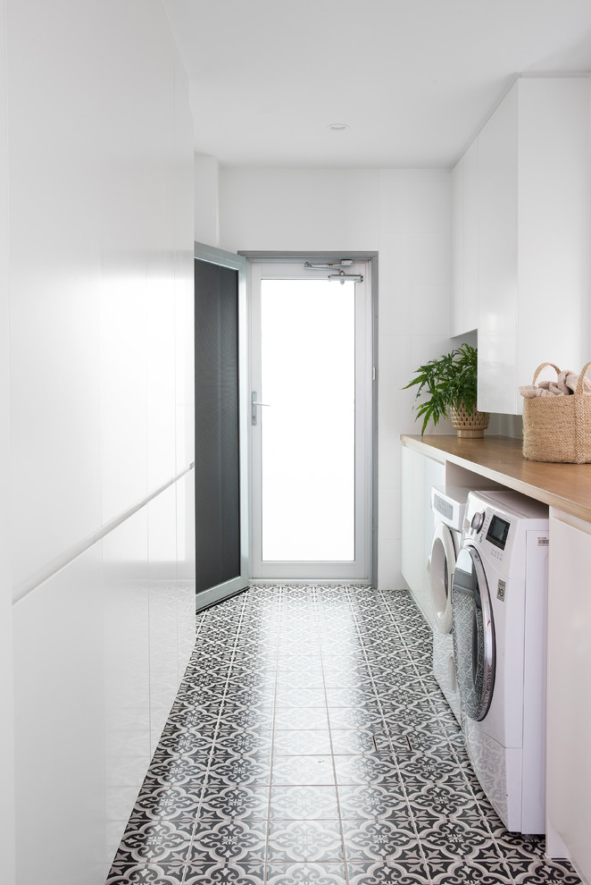 Inspiration for a mid-sized contemporary galley dedicated laundry room in Gold Coast - Tweed with flat-panel cabinets, white cabinets, wood benchtops, white walls, porcelain floors, a side-by-side washer and dryer, black floor and beige benchtop.