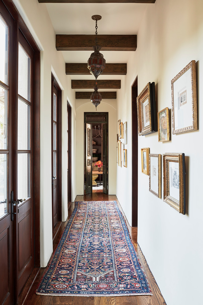 This is an example of an expansive mediterranean hallway in Los Angeles with white walls, dark hardwood floors and brown floor.
