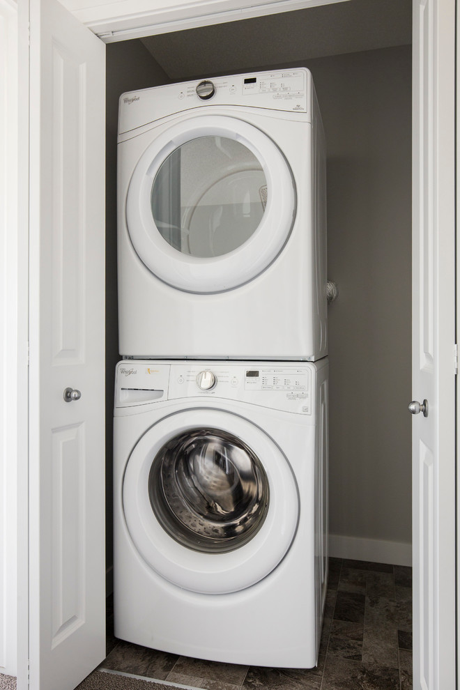This is an example of a small contemporary single-wall laundry cupboard in Calgary with a stacked washer and dryer.