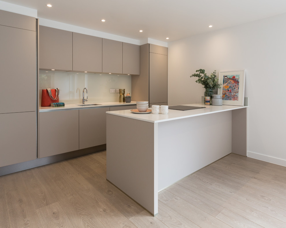 Mid-sized modern galley open plan kitchen in Gloucestershire with an undermount sink, flat-panel cabinets, brown cabinets, quartzite benchtops, glass sheet splashback, panelled appliances, laminate floors, no island, brown floor and white benchtop.