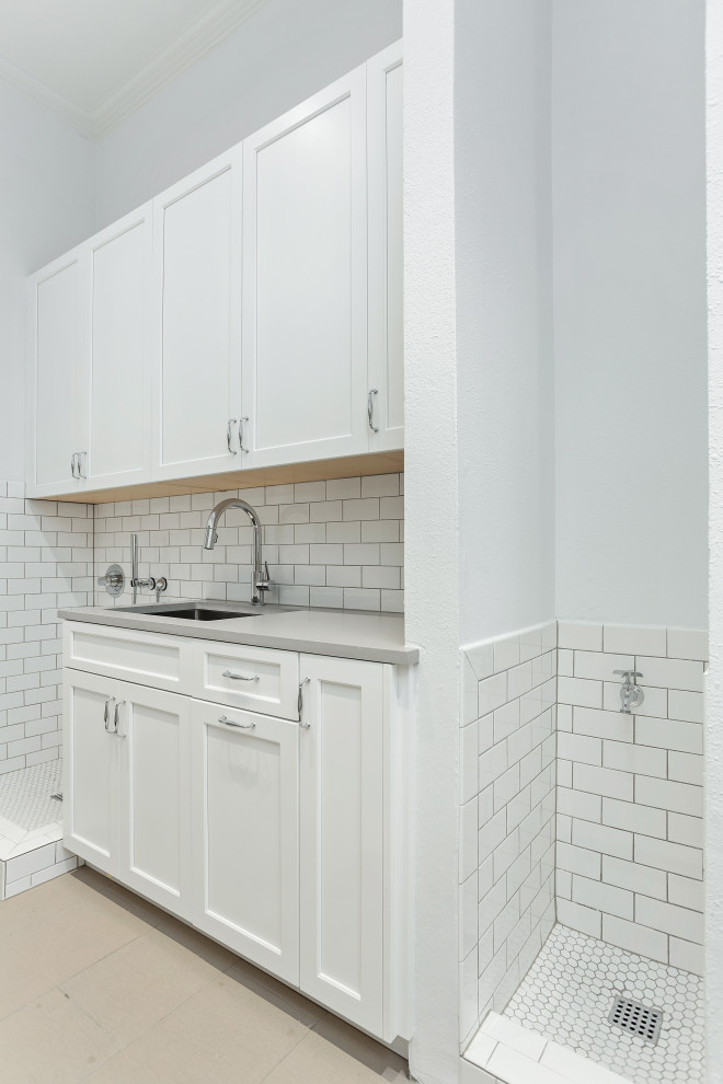 Large transitional galley utility room in Dallas with an undermount sink, recessed-panel cabinets, white cabinets, quartz benchtops, white splashback, ceramic splashback, white walls, porcelain floors, a side-by-side washer and dryer, beige floor, grey benchtop and decorative wall panelling.