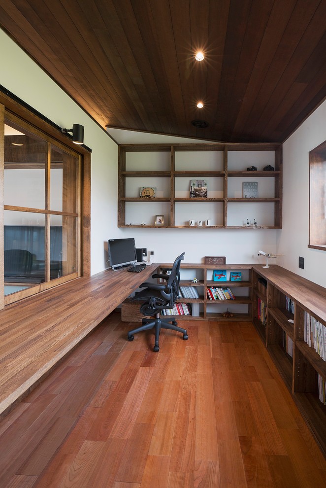 Asian home office in Other with white walls, medium hardwood floors, a built-in desk and brown floor.
