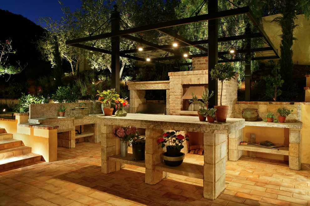 This is an example of a mid-sized mediterranean side yard patio in Orange County with an outdoor kitchen, tile and a pergola.